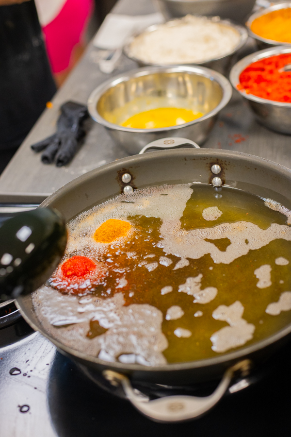 A pan of melted butter and oil with bright dollops of turmeric and chili spice, prep bowls in the background
