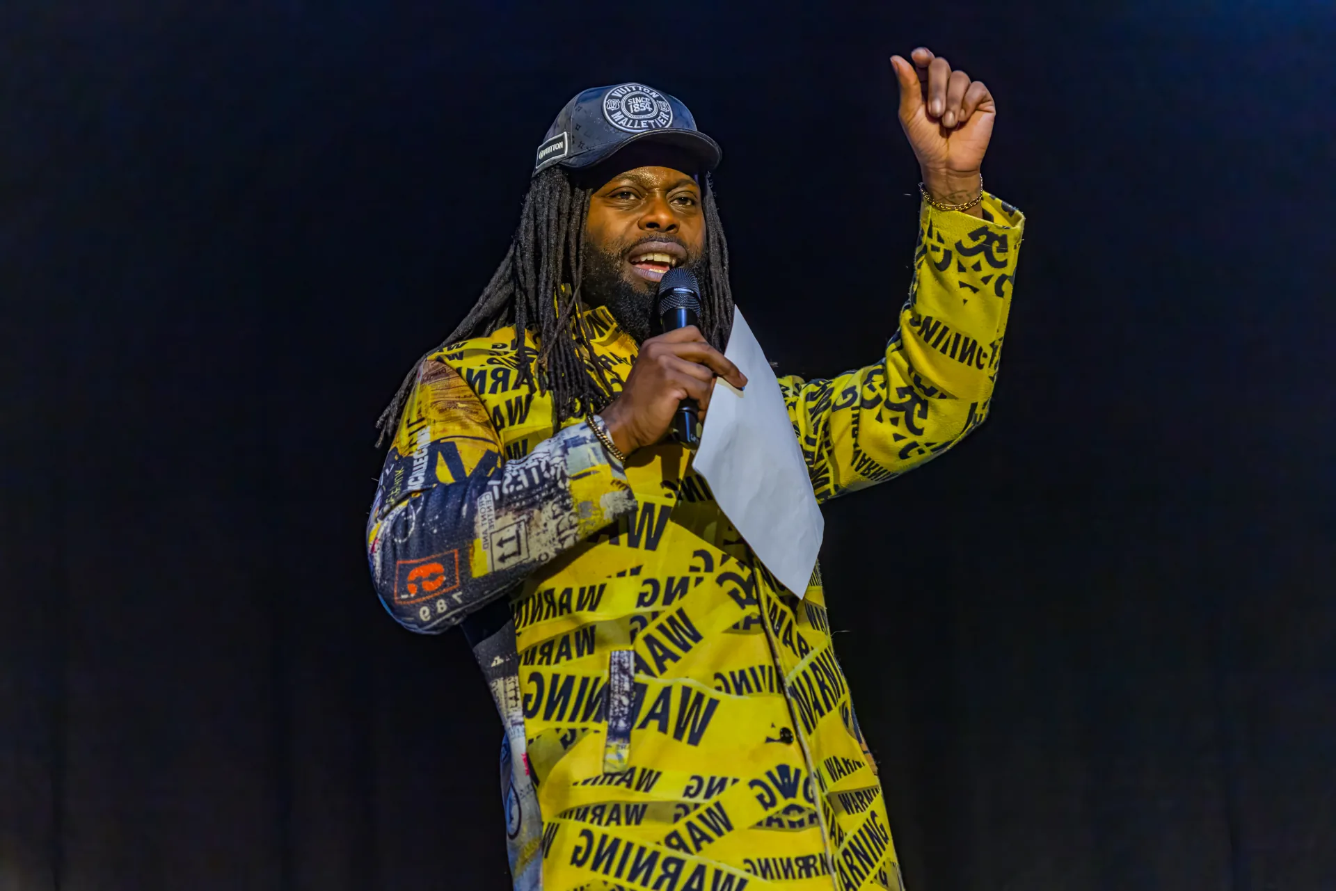 Host Keenan Krooner McClinton on stage in a bold yellow and black print outfit