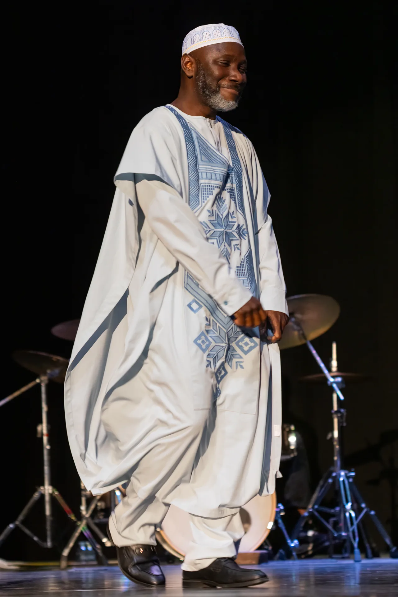 Man modeling a traditional white Agbada with blue geometric embroidery